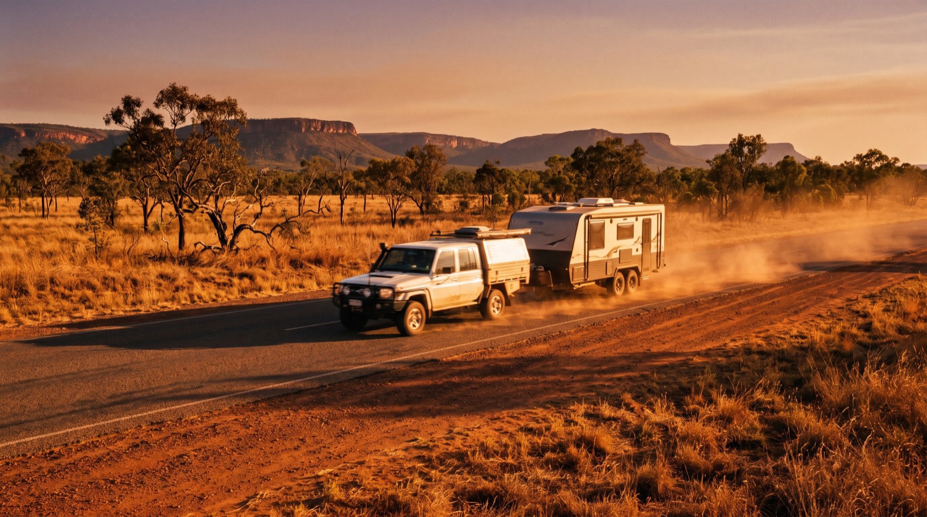 A four wheel drive towing a caravan along an inland Queensland highway at golden hour with dry grass and distant ranges
