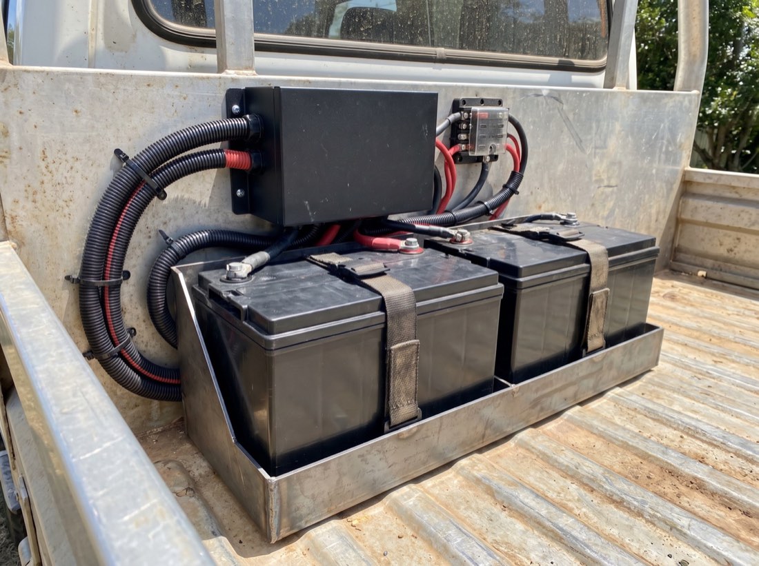 A dual battery setup strapped into a steel cradle in the tray of a four wheel drive with heavy red and black cabling
