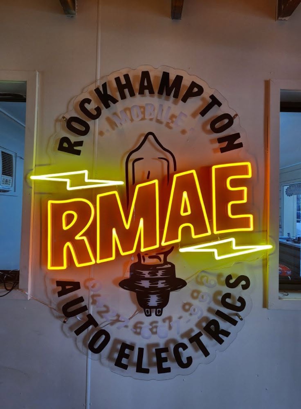 An illuminated RMAE sign mounted on the wall inside the Rockhampton Mobile Auto Electrics premises